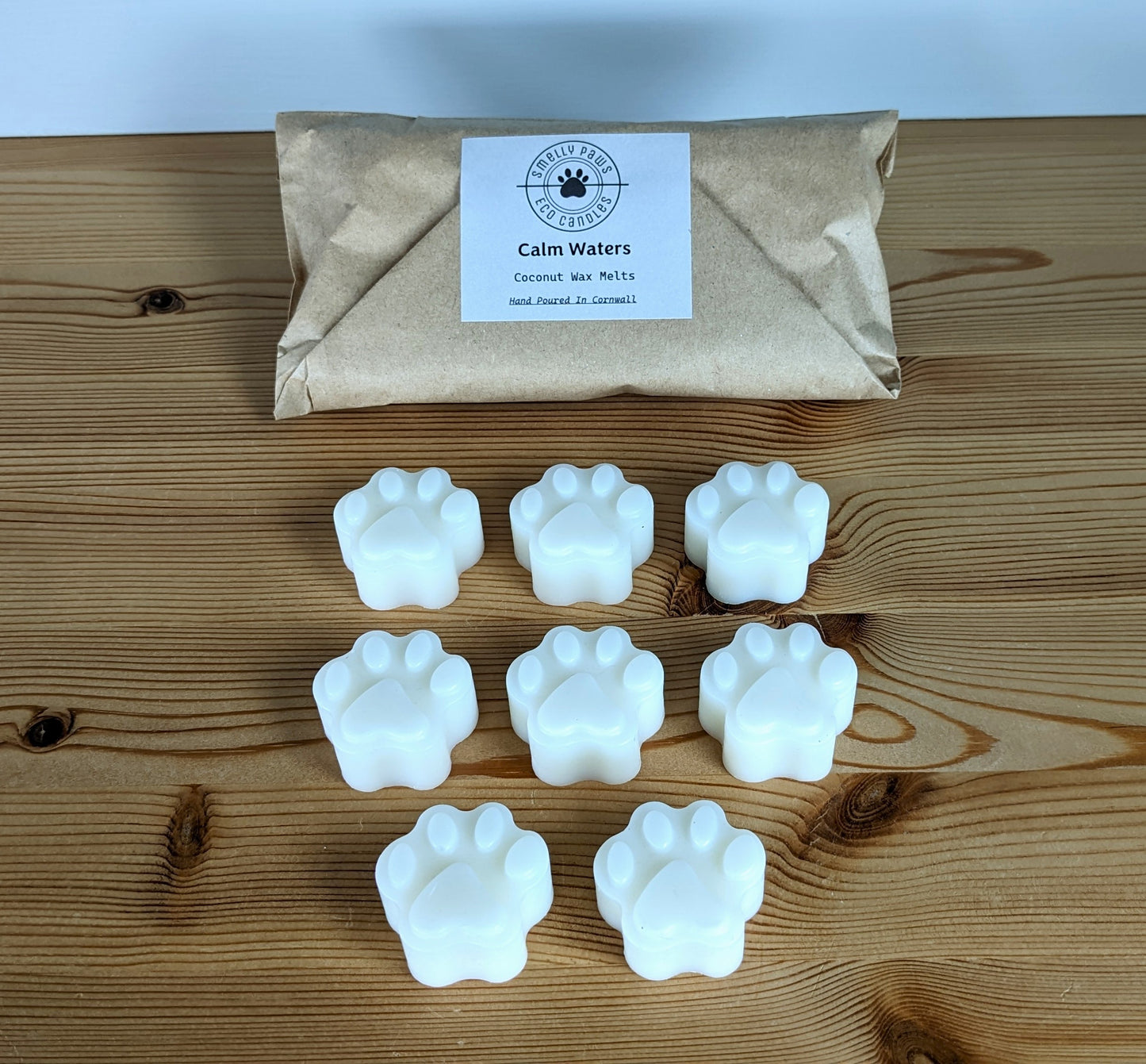 8 paw print wax melts sat on a wooden counter with a brown paper bag behind