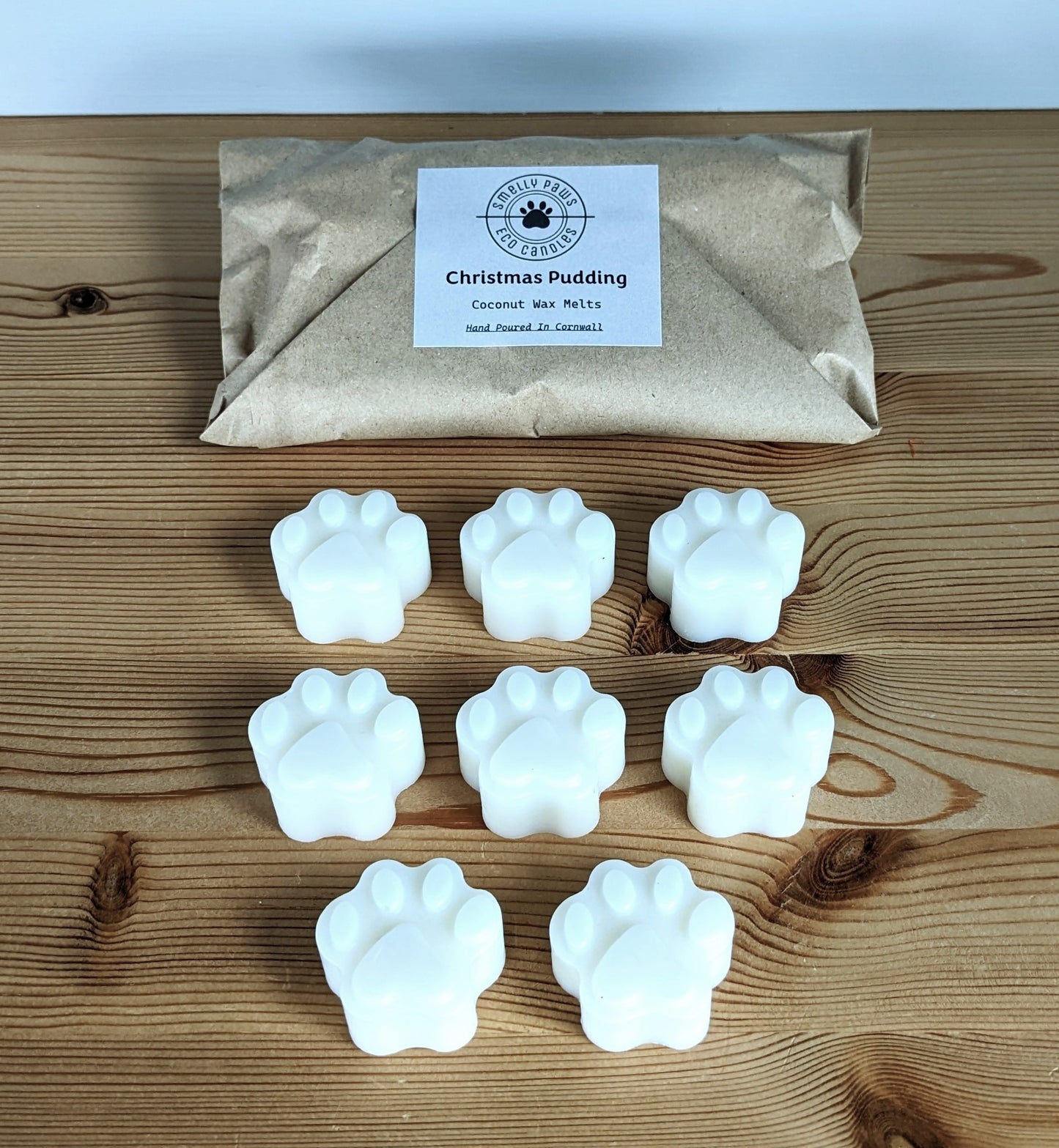 8 Paw print wax melts sat on a wooden counter with brown paper bag behind 