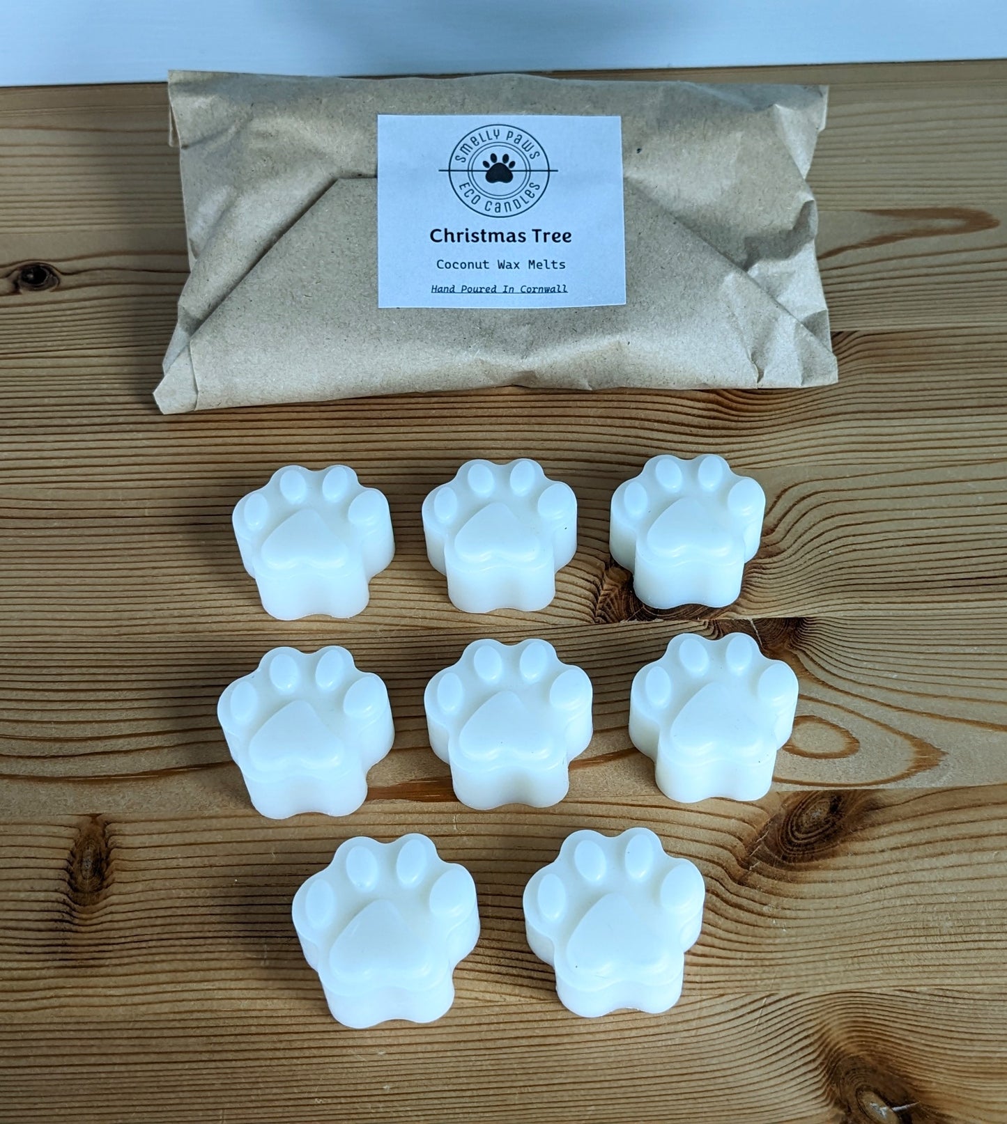 8 paw print wax melts sat on a wooden counter with brown paper packaging bag behind 