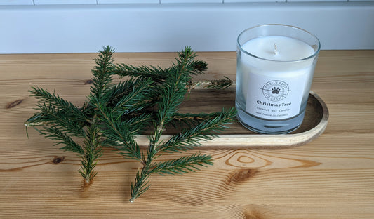 Christmas tree candle sat on a wooden tray with sprigs of fresh Christmas tree 