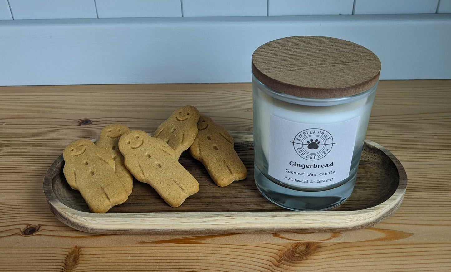 Gingerbread candle with wooden lid sat on wooden tray with 5 gingerbread men surrounding it