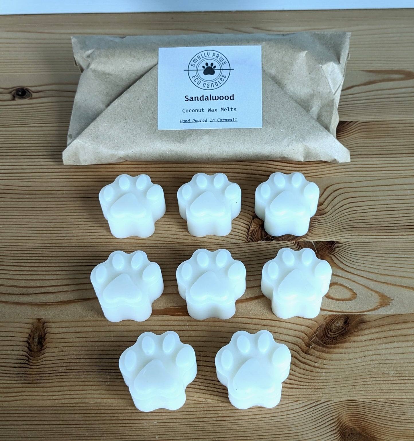 8 paw print wax melts sat on a wooden counter with a brown paper bag packaging behind 