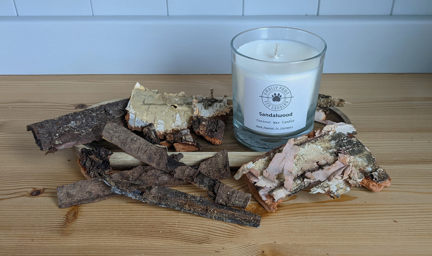 Sandalwood candle sat on a wooden tray surrounded by bark 