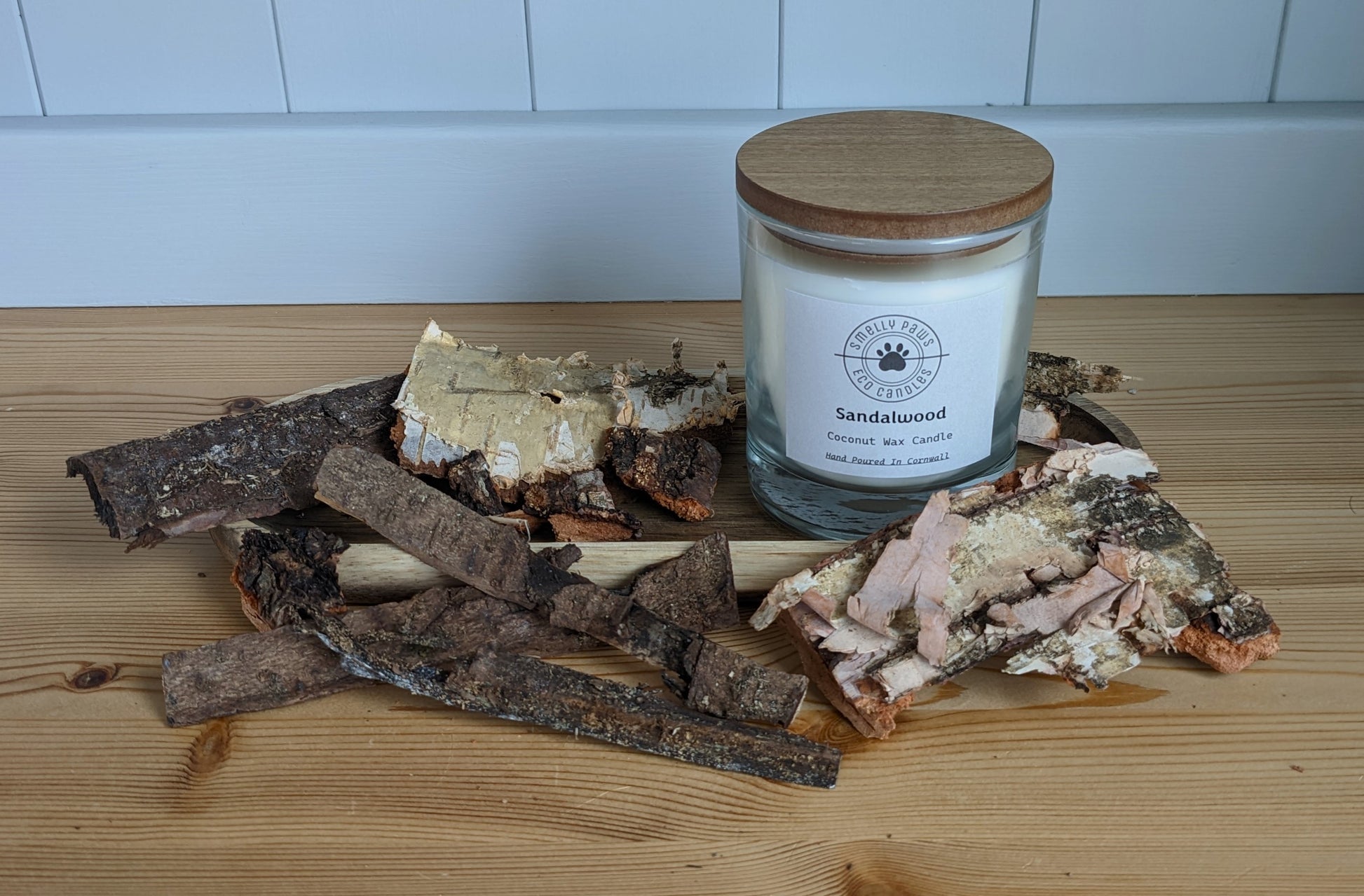 Sandalwood candle with wooden lid sat on a wooden tray surrounded by bark 