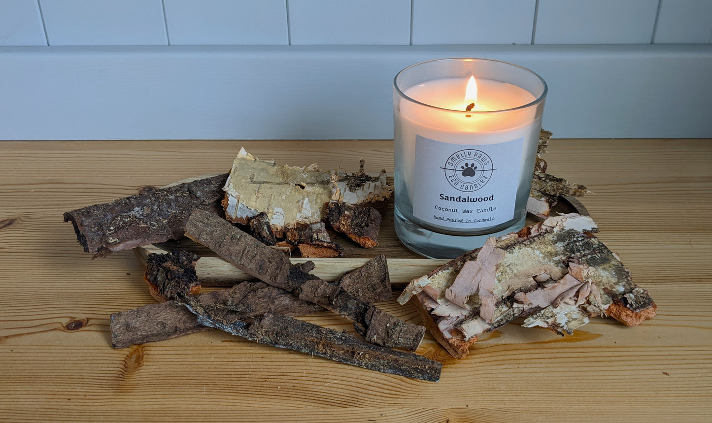 Burning Sandalwood candle sat on a wooden tray surrounded by bark 