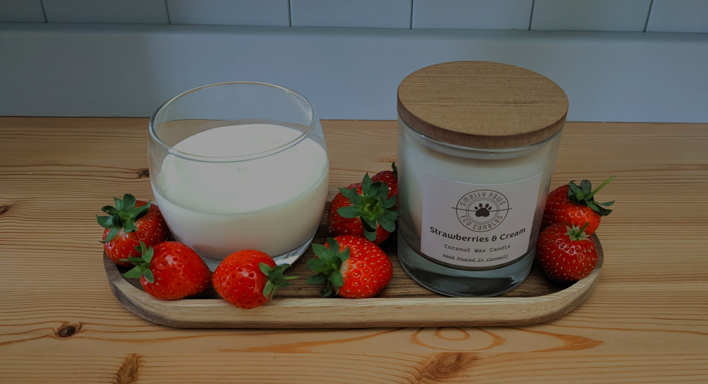 Strawberries and cream candle with wooden lid sat on a wooden tray with a pot of cream and surrounded by Strawberries 